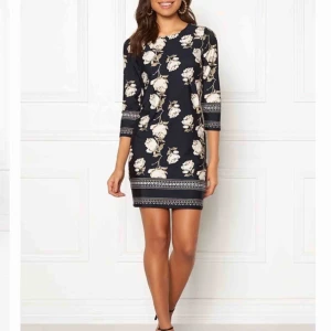 Mörk blå / blommig klänning  - Färg: Mörk blå / Mönster Material: 95% polyester, 5% elastan. Modellens längd & Storlek: 173cm | 32/34. Trikåklänning med skön passform och vackert mönster från HAPPY HOLLY. Stretchig, skrynkelfri trikå. 3/4-långa ärmar. Ofodrad.