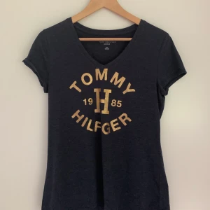 Tröja Tommy Hilfiger  - Marinblå t-shirt med guldglittrigt tryck från Tommy Hilfiger i nyskick. Classic fit i storlek S! 150kr + frakt 🪐