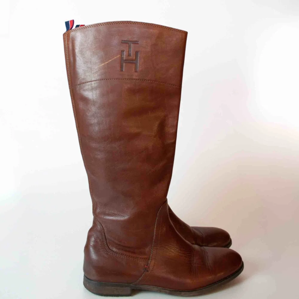 Tommy Hilfiger knee high real leather boots in brown size 39 A visible scratch on the right shoe, no anti slippery protection SIZE Label: 39 EU, feels like true to size Model: 163/38 (shoes) Measurements: Foot: 27 cm Ankle: 29 cm Shin: 40 cm Height: 41 cm. Skor.