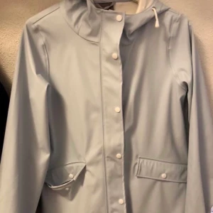 Regnjacka Vero Moda - Storlek S. Ljusblå regnjacka/regnkappa från Vero Moda. Använd några få gånger, nyskick! Stor luva, stora fickor. Tunt material. Knäppning med både dragkedja och knappar. Nypris 600 kr. 