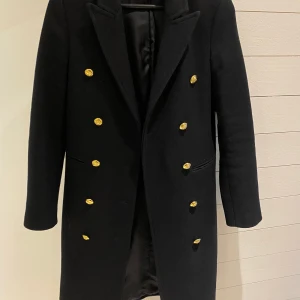 Svart kappa med guldknappar  - Otroligt stilig kappa från Zara med dekorativa guldknappar i fram och längst ärmslut. Passar perfekt nu till hösten och vintern. Kappan är i storlek xs och är som ny. 