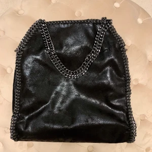 Stella McCartney väska - NY. Väska som liknar Stella McCartneys falabellaväska. Svart med mörka metallkedjor. Kan användas både med två korta eller en längre kedja. Aldrig använd. Köpt i Spanien. Mått: 38x41 cm. Köparen står för frakt. 🌟