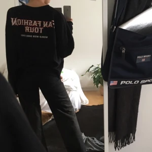  - Svart sweatshirt med text på ryggen och armen.