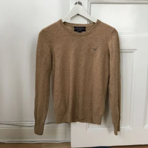  - Klassisk lammullströja från Gant. Kamel/sandfärgad. Skicket är perfekt. Värmer skönt i vinter!   Passar även XS och M beroende på hur man vill att den ska sitta på.   Skickas mot att köparen betalar frakten som går på 45kr.