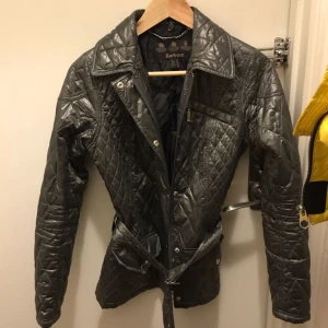  - Klassisk Barbourjacka med bälte i midjan. Grå glansig. Nyskick!