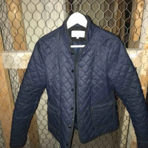  - Mörkblå quiltad jacka med svarta detaljer.