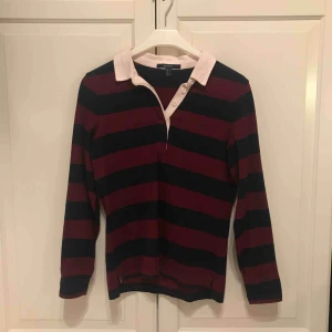  - Vinröd/marinblå-randig, långärmad piké-tröja från Gant. I fint skick. Storlek S. 