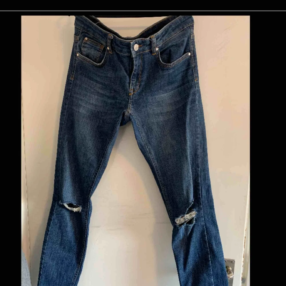 Blåa jeans med hål i båda knäna och slitningarna längst ner på byxorna.. Jeans & Byxor.
