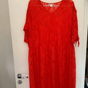  - Halvlång klänning, röd halvt genomskinlig med knyt på armarna.   Porto betalas av köparen. 