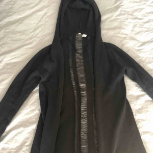  - Svart cardigan med huva. Detaljer/slitningar i ryggen. Slutar ungefär under rumpan. Knappt använd så fint skick! 