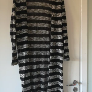 Lång stickad kofta.  - Lång, stickad kofta med slitsar i sidorna. Långärmad. Svart-och-vit-randig. Går ej att knäppa. 