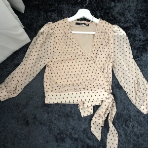 En beige wrap topp från Bikbok - En splitterny prickig wrap topp från Bikbok i väldigt skönt material. See through vid ärmarna men toppen i sig är inte see through vilket man nog tror av att titta på den då den är så skön och somrig. Skall knytas nedanför. Fina detaljer vid axlarna. 