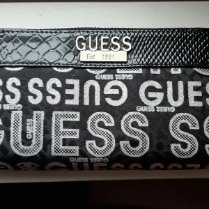 Guess Plånbok - Snygg helt ny Guess plånbok modell större. Svart med lack och silveraccenter. Köparen står för frakt. Fler bilder kan skickas vid intresse, 