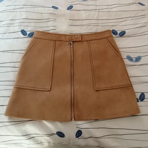  - Brun/beige kjol i mockaimitation, fodrad på insidan och går att öppna upp hela vägen. Aldrig använd då den är för stor. Möts upp i Stockholm eller skickas mot frakt. 