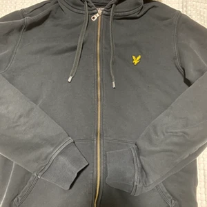 Lyles scout Hoodie/kofta - Svart Lyle scott kofta med huva och har en logotyp på vänster bröst. Modellen är i storlek M men passar för folk med S (Män) Varan är i bra form, 2 sidfickor i magen. Tillverkad med 100% bomull, tvättinstruktioner (maskintvätt)  