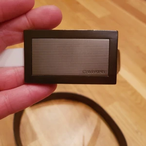 Calvin Klein  - Vändbart (svart på ena sidan och brunt på andra) skinnskärp stl 36, men går lätt att skrava av eller göra fler hål i. Oanvänt med taggar kvar. 6.5x3.7cm 