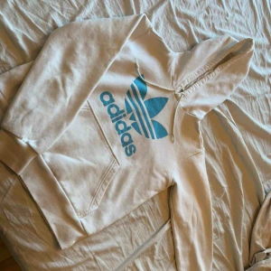  - Vit hoodie med blått tryck. Den är Fake, storlek 38