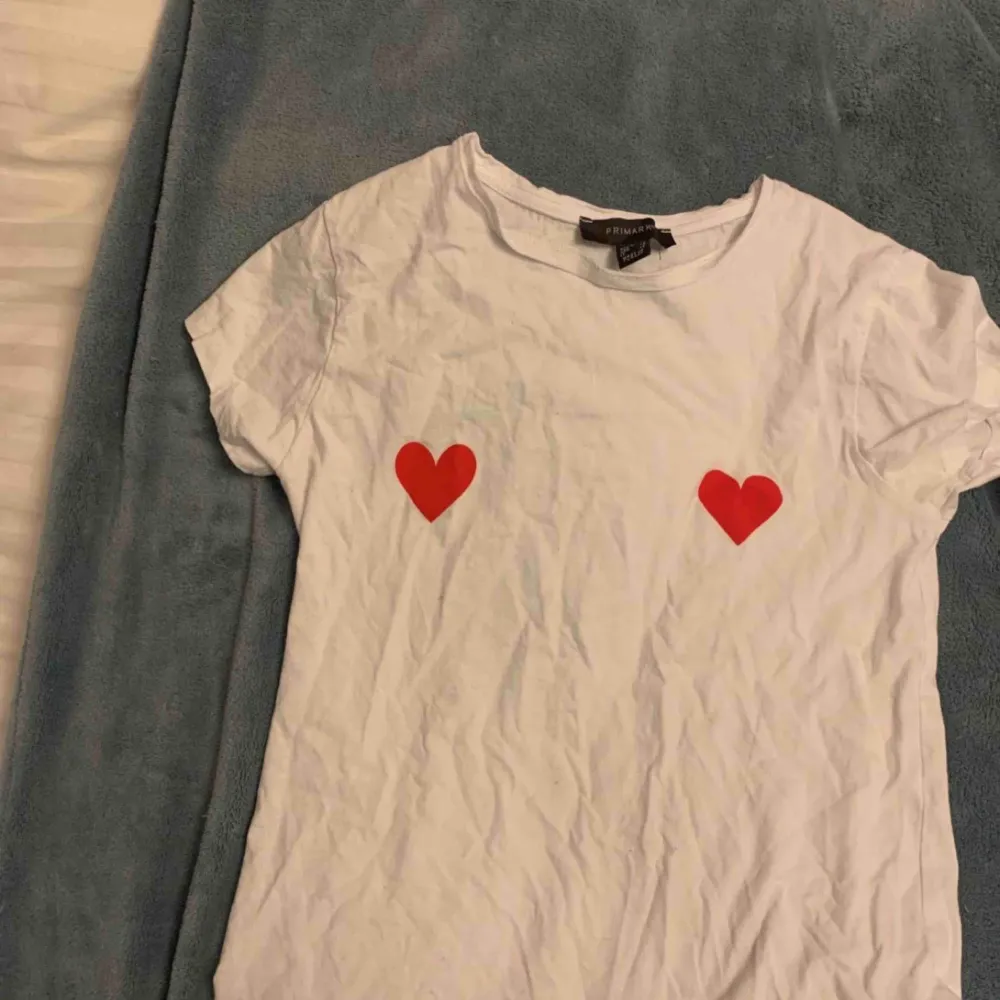 Vit T-shirt med två röda hjärtan som tryck. Tröjan är från primark och är i storlek XS/S. Använd 1-2 gånger, en gång ute och en gång hemma så skicket är som nytt. Helt felfri!. T-shirts.