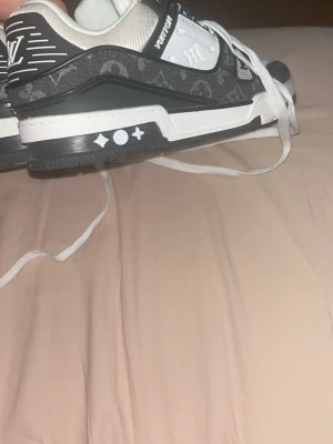 Louis Vuitton svarta sneakers - Louis Vuitton sneakers i svart och vitt med klassiskt monogrammönster och vita detaljer. Skorna har vita snören, låg profil och tydliga LV-loggor på hälen. Snygg kontrast mellan svart och vitt, perfekt för dig som gillar exklusiv streetwear.