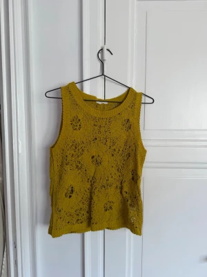 Zara - Gul stickad linnetopp - Säljer en gul stickad linnetopp med hålmönster och rund hals. Toppen är ärmlös och har en avslappnad passform, perfekt för varma dagar. Passar dig som gillar en unik och trendig stil.