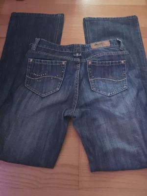Mörkblå bootcut jeans med nitar - Snygga mörkblå bootcut jeans med dekorativa nitar på bakfickorna och slitningar framtill. Klassisk femficksmodell med raka ben. Jeansen har kontrastsömmar och är tillverkade i denim med lätt stretch.
