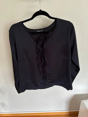 Marinblå blus med knytning från Missay - Stilren marinblå blus från Missay med långa ärmar och snygg knytning framtill. Blusen har rund halsringning och är gjord i ett mjukt, lätt material som ger en skön känsla. Perfekt för dig som gillar en enkel men trendig look.