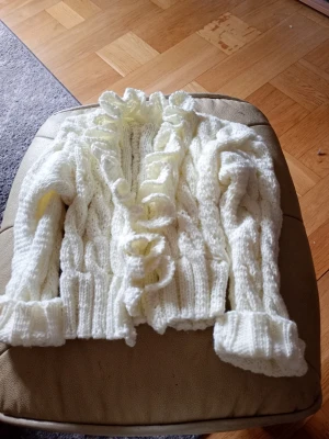 Baby/barn Vit stickad kofta med volang stl 6-12 månader  - Baby/barn Säljer en söt vit stickad kofta med volangkant längs öppningen och ribbade muddar. Koftan har ett kabelstickat mönster och är gjord i mjukt garn. Perfekt för dig som gillar romantisk och cozy stil.