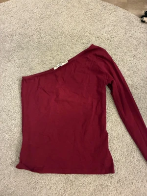 Vinröd oneshoulder topp från NA-KD - Säljer en vinröd oneshoulder topp från NA-KD i mjukt bomullsmaterial. Säljer då den är lite stor på mig. 