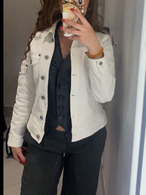 Vit jeansjacka med knappar - Snygg vit jeansjacka med klassisk krage och silverfärgade knappar framtill.