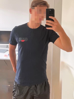 Mörkblå t-shirt från C.P. Company - Snygg mörkblå t-shirt från C.P. Company med rund hals och korta ärmar. På bröstet finns en liten patch med svart och rött broderi som ger en unik detalj. Storleken är i medium. Nypris 1199 mitt pris 630kr