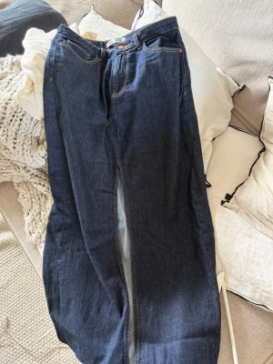Mörkblå lång jeanskjol med slits - Säljer en mörkblå lång jeanskjol i klassisk denim med hög midja och slits framtill. Kjolen har fickor både fram och bak samt bälteshällor. Perfekt för dig som gillar en tidlös och avslappnad stil.