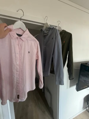 Ralph lauren skjorta - Säljer tre stilrena skjortor i rosa, ljusblått och olivgrönt med klassisk krage och broderad logga på bröstet. Alla har lång ärm och knappar framtill. Perfekta för en clean och tidlös look.                                                    Inprincip helt nya!