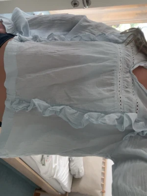 Ljusblå blus med volanger - Supersöt ljusblå blus med volangdetaljer och broderade hål längs bröstet. Blusen har långärmad design och är gjord i ett tunt, luftigt tyg som ger en romantisk vibe. Perfekt att styla med jeans eller kjol för en trendig look.Säljer för att jag har tröttnat på den!!! 💕💕💕