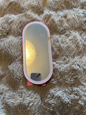 Söt rosa sminkspegel  - En oval sminkspegel med rosa ram. Perfekt storlek för sminkbordet eller att ta med i väskan. Spegeln har en enkel och lekfull design som passar dig som gillar söta detaljer.
