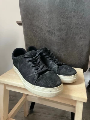 Svarta sneakers från Selected Homme - Svarta sneakers i mocka från Selected Homme med vita, tjocka gummisulor och svarta skosnören. Klassisk låg modell som passar till många olika stilar. Snygg och enkel design med rund tå och diskreta detaljer.