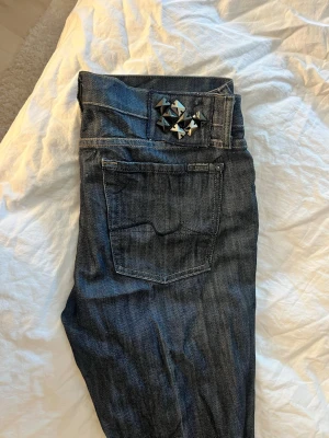 Mörkblå jeans  - Säljer ett par mörkblå jeans med botcut och coola  nitar vid midjan. Jeansen har klassisk femficksdesign och kontrastsömmar. Materialet är denim i bomull och passformen är rak. Perfekta för dig som gillar detaljer och en edgy stil. Orginal pris 3000