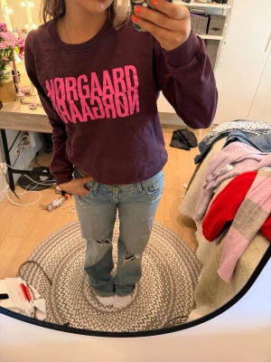 Lila sweatshirt från Nørgaard - Cool lila sweatshirt från Nørgaard med stor rosa logga framtill. Tröjan har en avslappnad passform, rund halsringning och långa ärmar. Perfekt för en casual look och enkel att matcha med jeans eller kjol.