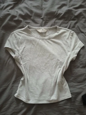 Vit kortärmad t-shirt från H&M - En enkel och stilren vit t-shirt från H&M med rund hals och korta ärmar. Tillverkad i mjuk bomull som känns skön mot huden. Passformen är något figurnära och toppen är perfekt att matcha med jeans eller kjol.