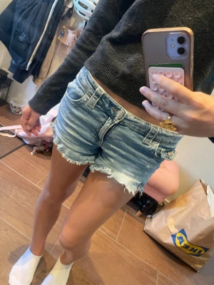 Ljusblå jeansshorts med rå kant - Säljer ett par ljusblå denimshorts med rå, fransig kant och klassisk femficksdesign. Shortsen har normal passform och låg midja, samt slitningar för en avslappnad look. Perfekta för varma dagar och enkel att matcha med olika toppar. Sitter som xs/s