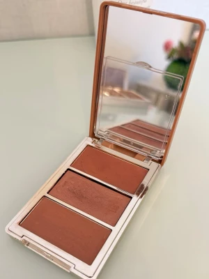Morphe Cheek Thrills Multi-Finish Face Trio  - En smidig och kompakt rougepalett från Morphe med tre olika nyanser och finishar i varma, bronziga och bruna toner (nyans: After Party). Paletten innehåller en inbyggd spegel och ger möjlighet att bygga upp och blanda färgerna för en solkysst och naturlig lyster på kinder och ansikte. Användning: inte mer än 3 gånger.