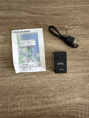 GPS-spårare GF-07 med USB-kabel - Säljer en kompakt svart GPS-spårare modell GF-07. Medföljer gör en USB-laddningskabel och en enkel manual. Perfekt för att hålla koll på fordon eller andra värdesaker. Enheten är rektangulär och har tydlig märkning på ovansidan. Behöver SIM-kort. 