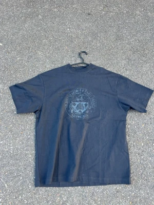 Svart balenciaga t-shirt med tryck - Cool svart t-shirt med ett slitet tryck framtill som har text och emblem. T-shirten har rund hals och korta ärmar, perfekt för en avslappnad stil. Materialet känns som bomull och passformen är normal.