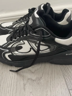 Svarta och vita sneakers med grafiskt mönster - Snygga sneakers i svart och vitt med grafiskt mönster på sidorna. Skorna har tjock sula, svarta snören och meshdetaljer för extra ventilation. Perfekta för dig som gillar en sportig och modern look.