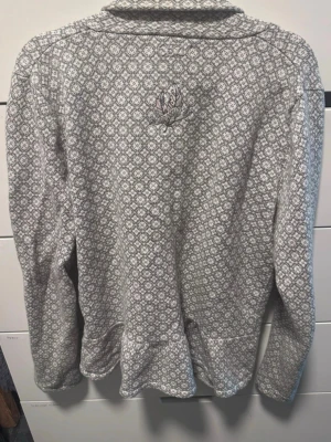 Mönstrad stickad tröja Odd Molly - Gråmelerad stickad tröja från Odd Molly med diskret vitt och ljusrosa mönster. Tröjan har långa ärmar och en broderad detalj med fjädrar och logga på ryggen. Perfekt för dig som gillar unika detaljer och skön passform.