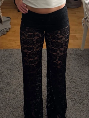 Svarta utsvängda spetsleggings - Säljer ett par svarta leggings i genombruten spets med blommönster och utsvängda ben. Låg midja och stretchigt material som sitter snyggt på kroppen.  Aldrig använda 
