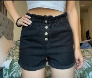 Svarta jeansshorts med knappar från Chiquelle - Svarta jeansshorts från Chiquelle i storlek 34. Använda ett fåtal gånger men är i nyskick. Lagom långa på mig som brukar ha xs-s och är 173cm lång. Fickorna går att använda och shortsen knäpps genom de fyra knapparna framtill. Sitter skönt i midjan.