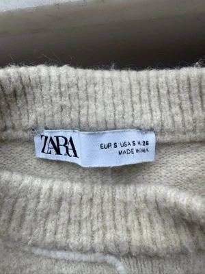 Beige stickad tröja från Zara - Mysig beige stickad tröja från Zara med rund halsringning och ribbade muddar. Tröjan har en enkel och clean design som passar perfekt till många olika outfits. Materialet känns mjukt och skönt mot huden.
