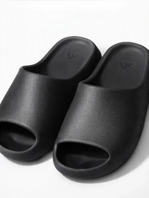 Svarta chunky tofflor i skum - Säljer ett par svarta chunky tofflor med öppen tå och bred rem. Tillverkade i mjukt och flexibelt skummaterial för extra komfort. Minimalistisk design med diskret logga på innersulan. Perfekta för att glida runt hemma eller på stranden.