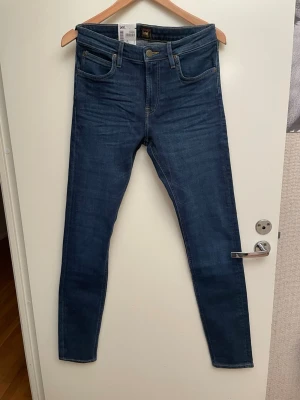 Mörkblå skinny jeans från Lee, stl W29/L34 nya - Snygga mörkblå skinny jeans från Lee med klassisk femficksdesign och guldfärgade detaljer. Jeansen har hög midja och smal passform hela vägen ner. Perfekta för dig som gillar en stilren och tidlös look.
