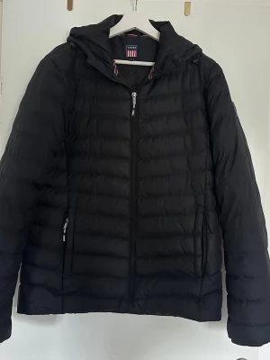 Svart pufferjacka från Vinson - Säljer en svart pufferjacka från Vinson med huva och dragkedja framtill. Jackan har två sidofickor med dragkedja och quiltad design som ger en sportig look. Perfekt för kalla vinterdagar och riktigt skön att bära.